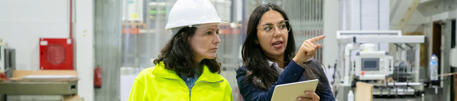 one woman in a hard hat and one woman with laptop walking through factory floor conducting an energy analysis